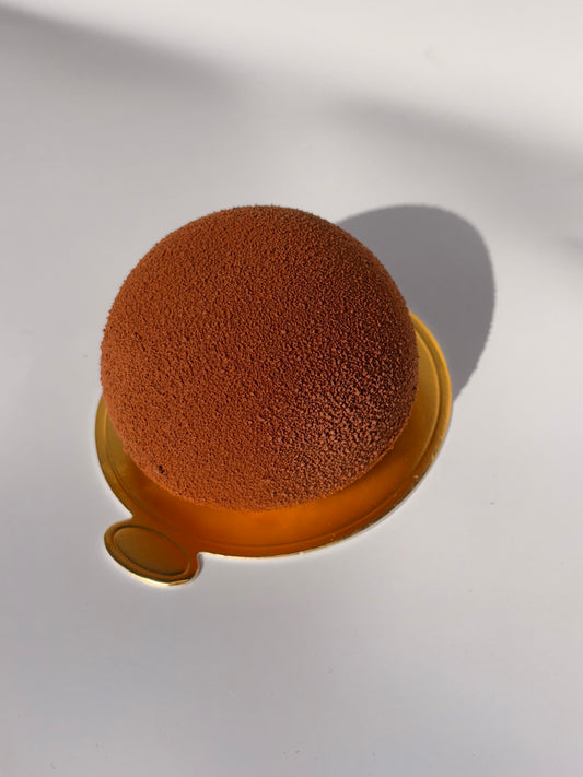 En rund brun mini entremet med sammetsyta serverad på guldig bricka – Ganache Cakery Malmö.

A round brown mini entremet with velvet surface served on a golden tray – Ganache Cakery Malmö.

Un mini entremet rond brun à texture veloutée, servi sur un plateau doré – Ganache Cakery Malmö.